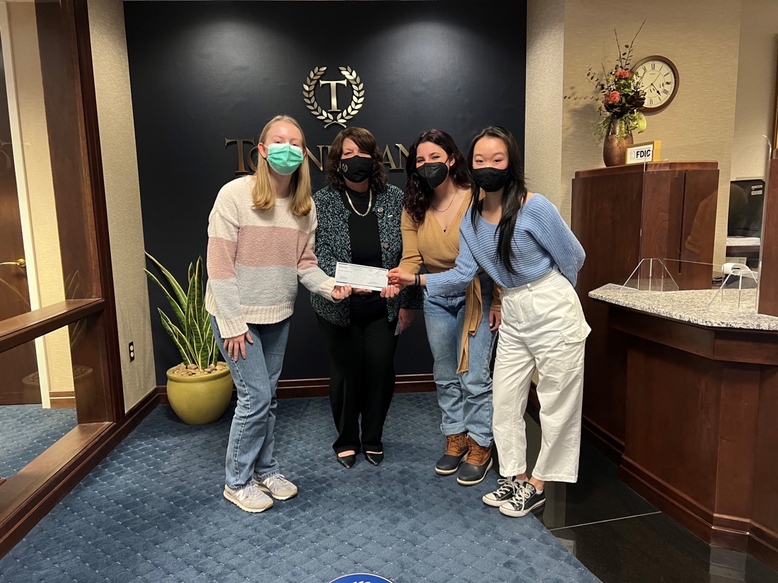 Four people posing in an office and holding a small donation check.