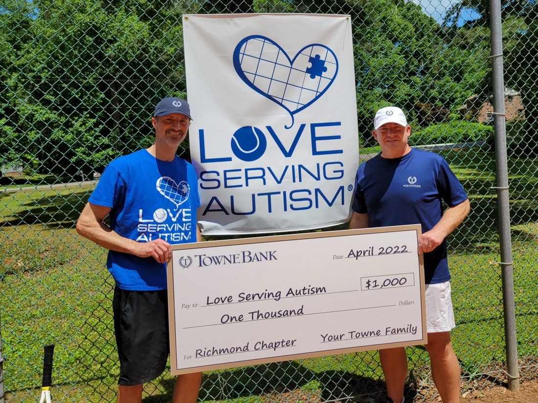 Two people standing in front of a fence and holding a large donation check.